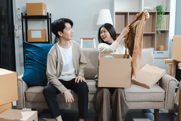 Young couple relaxing sitting on the sofa using the computer laptop around cardboard boxes, very happy moving to a new house.