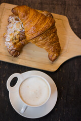 Croissant and cup of hot cappuccino On black wooden desk at breakfast.