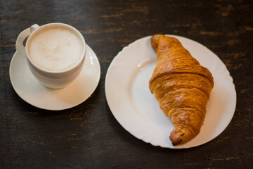 Croissant and cup of hot cappuccino On black wooden desk at breakfast.