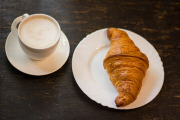 Croissant and cup of hot cappuccino On black wooden desk at breakfast.