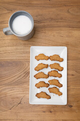 Car-shaped homemade oatmeal cookies on a white tray with a cup of milk