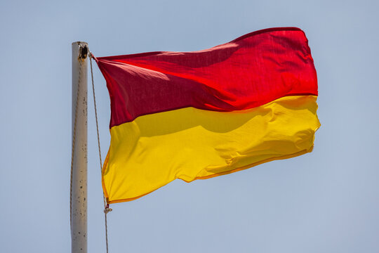 Red and yellow warning beach flag is under blue sky