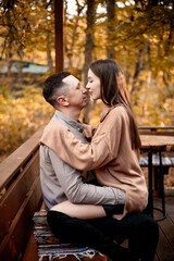 a young couple guy with a girl in autumn in a cafe in brown and orange tones on an outdoor terrace hugging and kissing, love or Valentine's day