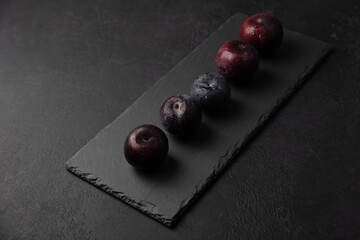 Juicy ripe fresh plum with water drops on black slate board. Seasonal fruit on black background. Selective focus, close-up.