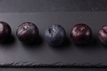 Juicy ripe fresh plum with water drops on black slate board. Seasonal fruit on black background. Selective focus, close-up.