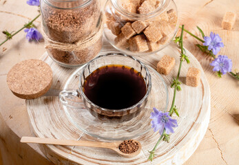 Cup chicory tea, jars of granulated soluble chicory and cane sugar, spoon on wooden stump.