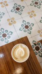 Top view of a cup of hot cappuccino on a wooden table with beautiful floor tiles in the background