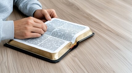 Naklejka premium Hands gently clasped over an open Bible on a table, accompanied by a cup, conveying a moment of reflection and tranquility in soft, natural light