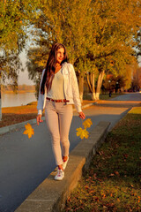 young beautiful girl walking on concrete parapet in autumn park in rays of sunlight