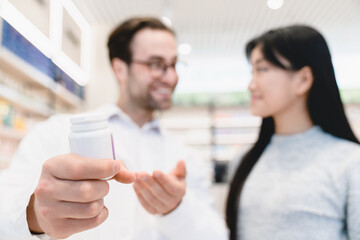 Obraz premium Closeup cropped shot of focused medicine jar with drugs, vitamins, pills, painkillers, antibiotics while male caucasian pharmacist showing advising medications to female client customer