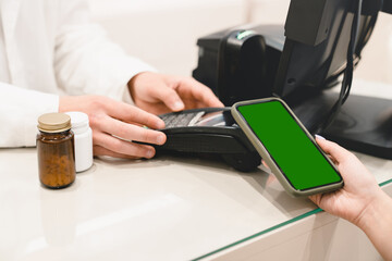 Cashless wireless payment with mobile phone cellphone with mockup, green screen, copyspace at drugstore pharmacy at cash point desk, buying medicines, drugs, pills with credit card.