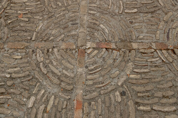 Close-up of a stone pavement featuring a circular brick pattern embedded in cement. The intricate design highlights the texture and craftsmanship of this flooring. Background image