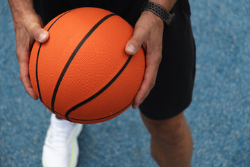 Basketball orange ball in man hand on blue court. Summer outdoor game. Sport background. Close up.