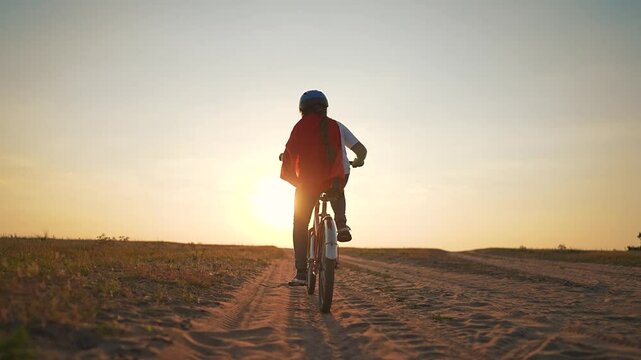 Child superhero cape rides bicycle at sunset feeling freedom and adventure. child pedals bicycle embracing superhero role. Imaginative play brings freedom as child dreams heroic adventures on bicycle.