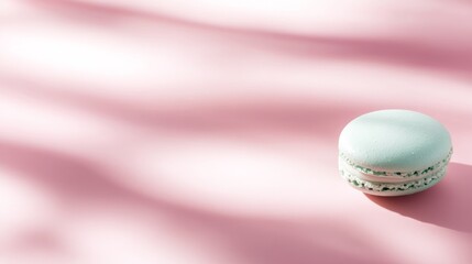 Obraz premium A mint green macaron rests against a gentle pastel pink background, accented by subtle shadows that enhance its delicate texture and vibrant color, creating a visually appealing contrast