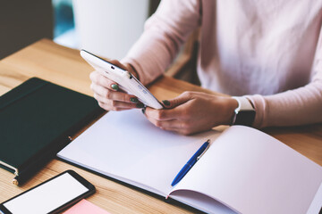 Cropped image of female hands holding modern touchpad and typing text email with answer about price of online language courses, woman planning week with knowledge textbook and digital technologies