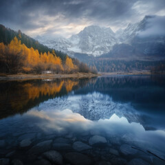 Fototapeta premium A serene landscape showcasing a crystal-clear lake reflecting snow-capped mountains with vibrant golden autumn trees surrounding the water. 