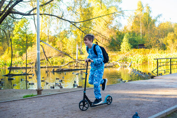 boy riding scooter on bridge, through autumn park