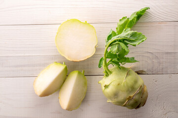 One whole ripe kohlrabi and one cut lie on a wooden table, macro, top view.