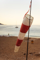 A colorful red and white wind vane is hanging from a tall pole on the beach