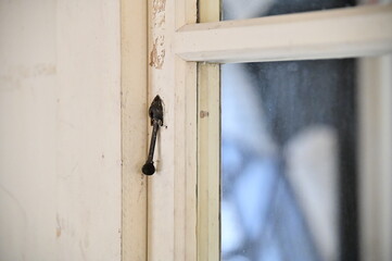 A side angle captures the iron lock on a white-painted wooden window with glass panes. The glass reflects light from within, creating a soft glow that contrasts the rustic lock.