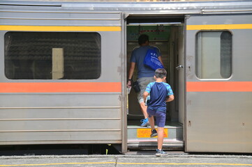 Taiwan - Sep 17, 2024: On a sunny summer day, a man and a boy prepare to board a Taiwan Railway train, with the man inside and the boy stepping up.