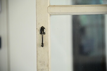 A detailed shot of an iron lock affixed to a white-painted wooden window with glass panes. The rustic lock adds a vintage charm to the clean, polished look of the window frame.