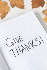 Give thanks, handwriting in notebook with autumn leaves on white background. Close-up. Thanksgiving...