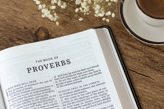 Proverbs open holy bible book with coffee cup on wooden desk. Studying and reading old testament Scripture, wisdom from God Jesus Christ, Christian biblical concept.