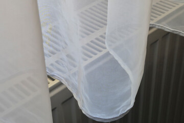 A close-up of soft, sheer curtains gently draping over a radiator, creating a cozy and airy...