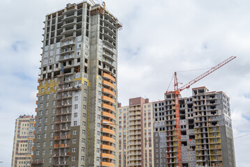 Fototapeta premium A tower construction crane next to a high-rise building under construction. The frame of the building under construction next to the crane. The structure of the building is made of reinforced concrete