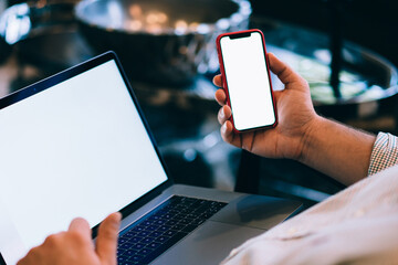 Back Close up of caucasian young man holding blank display mobile phone in hands, verification of banking data, shopping online on laptop computer and cellphone with mock up screen for web advertising