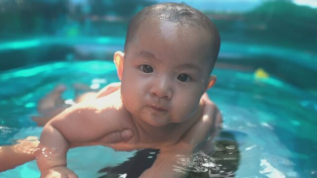 Adorable smiling baby girl swims in swimming pool with sparkling lights shining on the water.