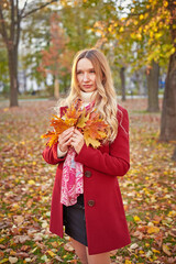 Naklejka premium A woman in a red coat and a black skirt walks in an autumn park. The concept of autumn and the beauty of nature.