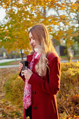 A woman in a red coat and a black skirt walks in an autumn park. The concept of autumn and the beauty of nature.