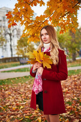 A woman in a red coat and a black skirt walks in an autumn park. The concept of autumn and the beauty of nature.