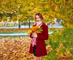 A woman in a red coat and a black skirt walks in an autumn park. The concept of autumn and the beauty of nature.