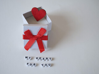 Auf einem hellen Hintergrund steht eine weiße geöffnete Schachtel mit einem roten Herz, auf dem...