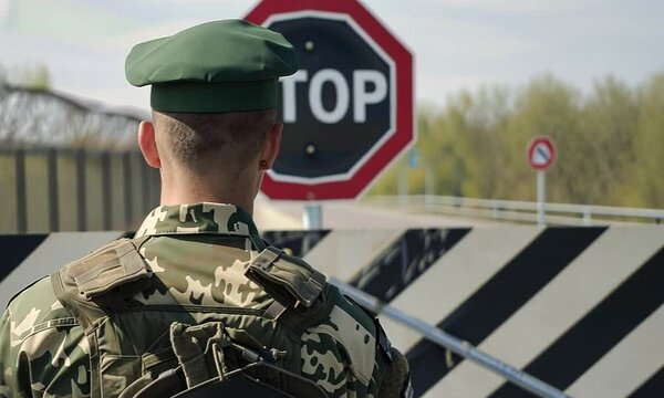 A soldier in uniform watches over a border checkpoint, reflecting vigilance and duty. The iconic stop sign emphasizes the importance of security in this serene yet significant setting