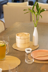 Fototapeta premium Dining table with bamboo steamer, vase with bamboo plant, and lemonade pitcher