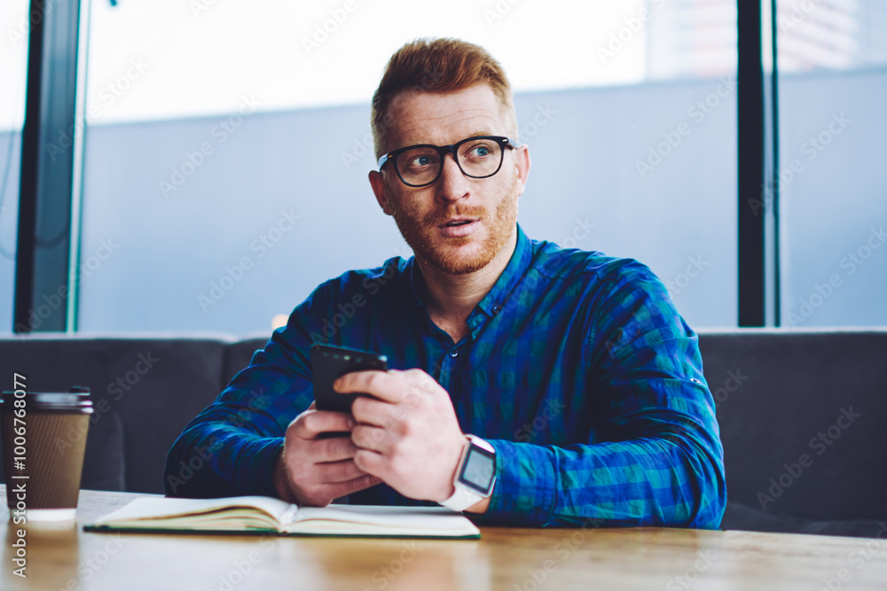 Poster pondering hipster guy in spectacles thoughtful looking away while waiting for call from customer ser