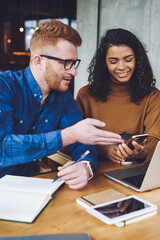 Happy smiling male and female hipsters reading received email via modern smartphone gadget during planning organisation of event with friends in coffee shop, concept of technology and communication