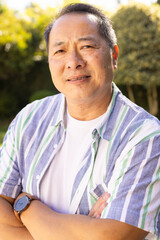 Smiling asian middle-aged man in striped shirt standing outdoors, enjoying sunny day