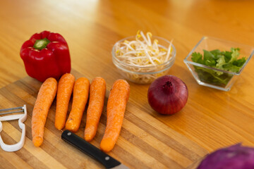 Preparing fresh vegetables, cutting carrots, bell pepper, and onion on wooden cutting board