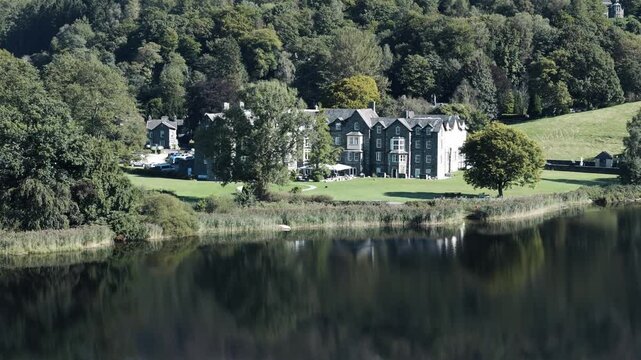 Aerial establishing orbit of Grassmere Lake and lakeside hotel with reflection of building and trees shimmering in water