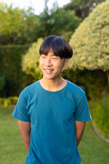 Smiling young asian teenage boy in blue shirt standing in garden, enjoying outdoor time