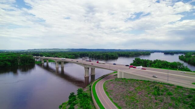 Aerial view of a red semi-truck with a step deck low boy trailer and a dry van trailer crossing the Dresbach Bridge over the Mississippi River at the border of Minnesota and Wisconsin.