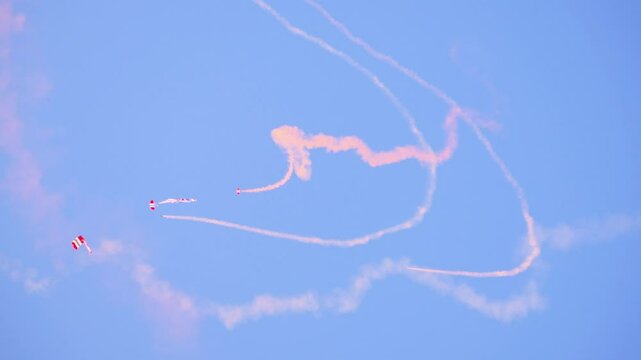 British Red Devils parachutists perform intricate maneuvers, leaving vibrant smoke trails in the sky during a military display. Captured mid-air with clear blue skies. Ginkelse Heide, Ede, Netherlands