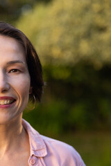 Fototapeta premium Smiling middle-aged woman with short hair wearing pink shirt and hoop earring outdoors, copy space
