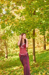 A woman in a red dress walks through an autumn park with leaves on the ground. The leaves are yellow and brown, and the woman is wearing a red dress.